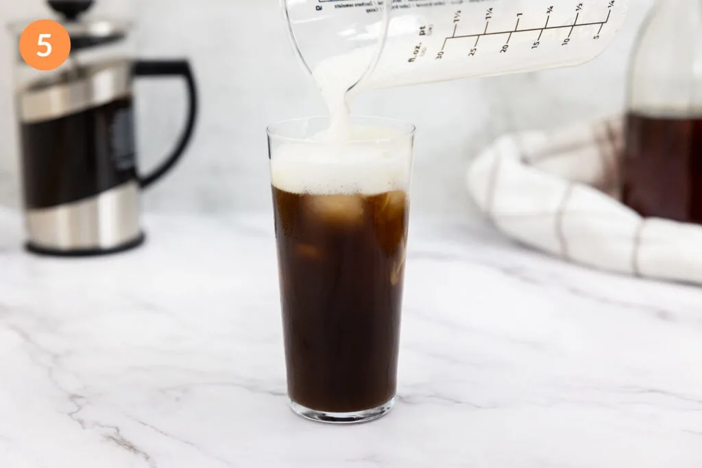 Pouring cold foam on to a cold brew in a glass