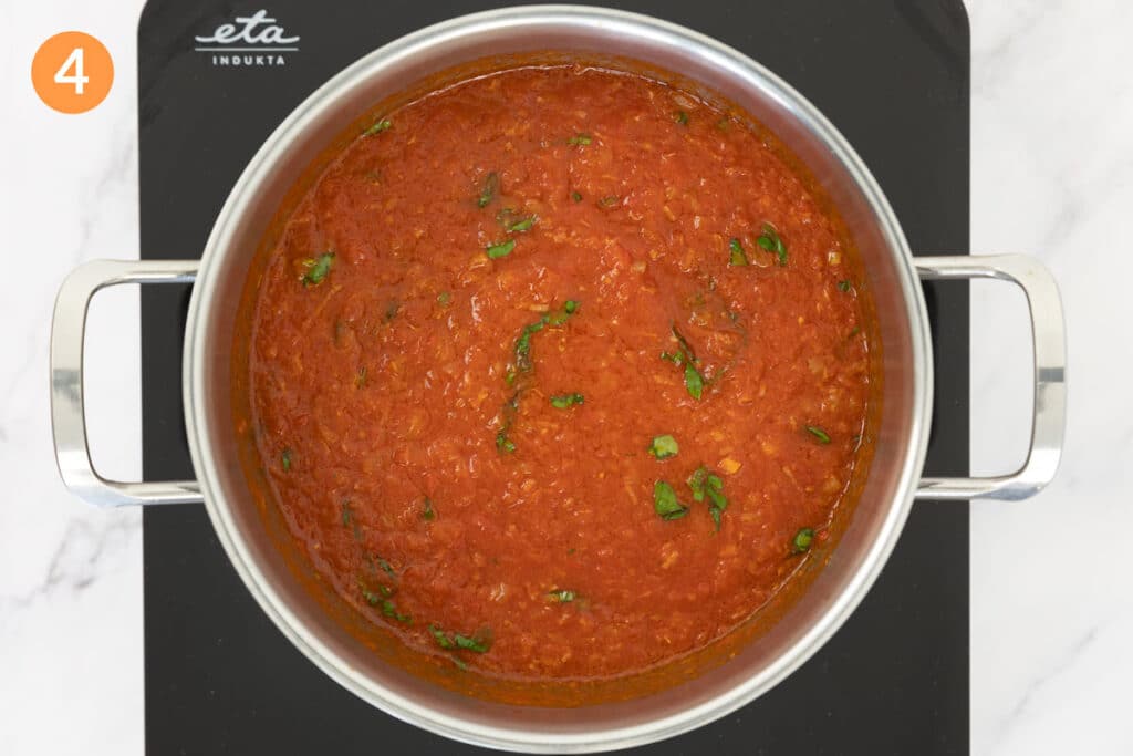 Simmered tomato sauce that has been mixed with fresh basil in a large pot