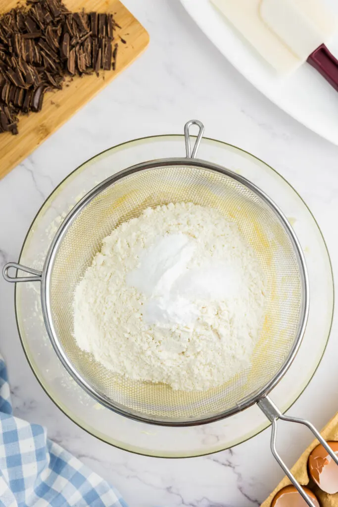 Flour, baking powder, baking soda and sea salt being sieved into the butter sugar mix