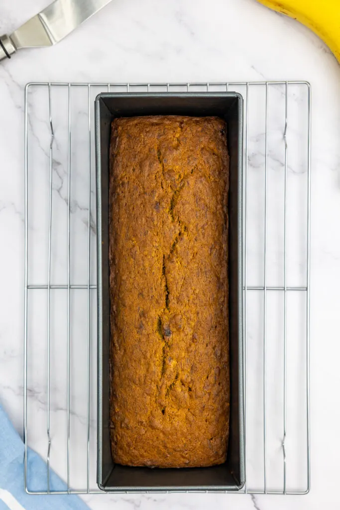 Cooked banana bread in a loaf pan on a cooling rack