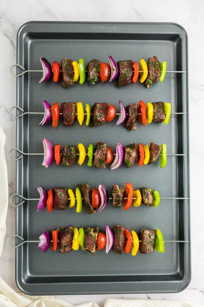 Beef steak and vegetables skewered and placed onto a baking tray