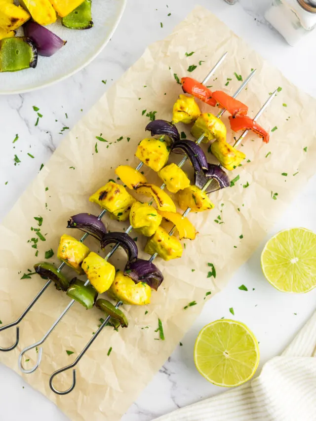 Chicken kabobs on metal skewers next to lime