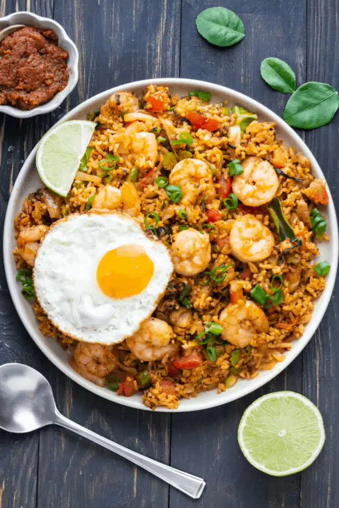 Tom yum fried rice on a white plate with lime and a fried egg