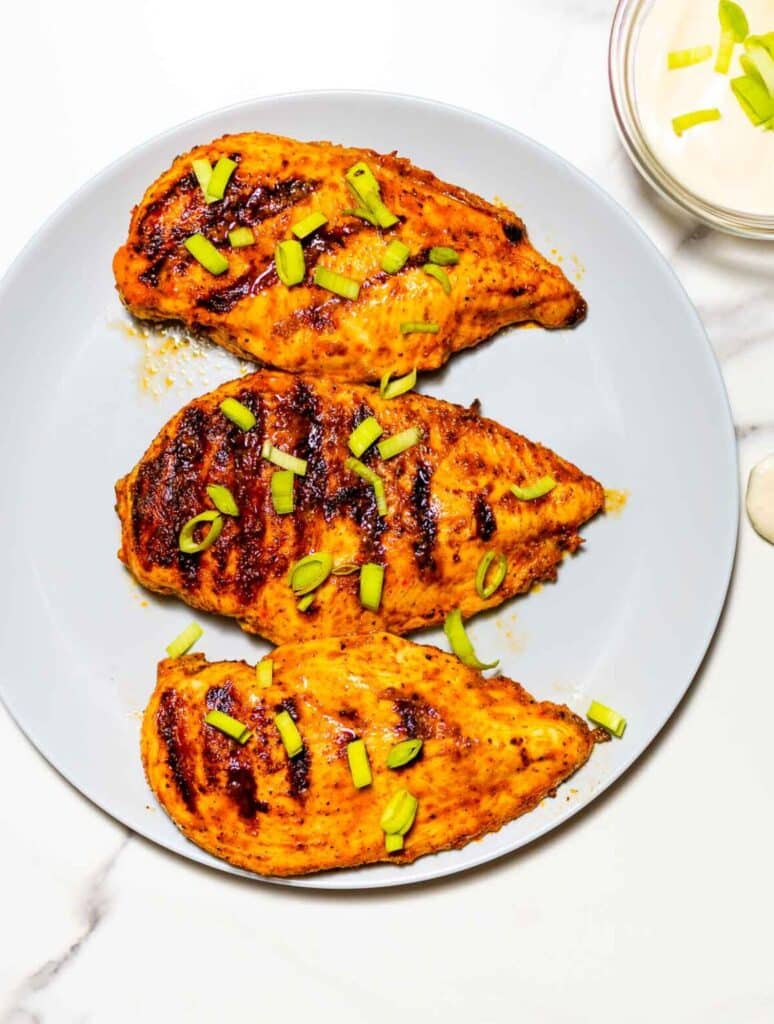 Grilled buffalo chicken on a white plate with scallions 