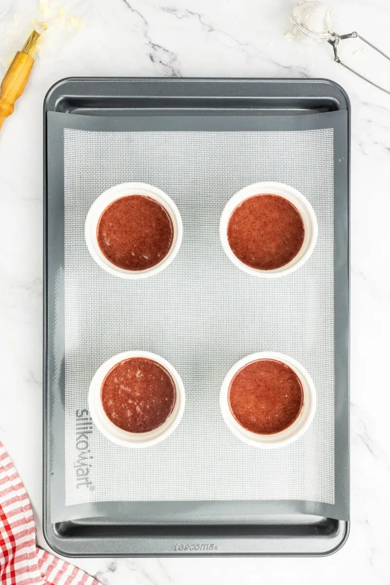 Red velvet lava cake batter in ramekins on a baking tray