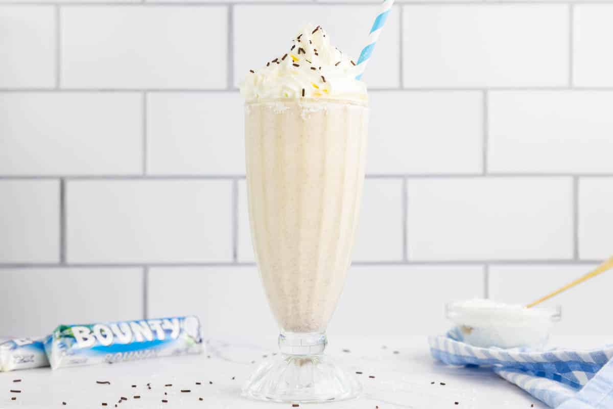 Bounty milkshake in a milkshake glass with a blue straw and bounty chocolate bars in the background