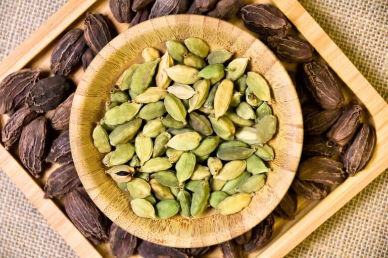 Green and black cardamom in dishes on a table.