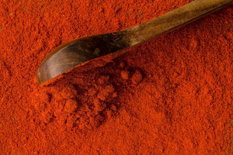Kashmiri red chili powder on a surface with a wooden spoon.
