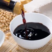 A bottle of dark soy sauce being poured into a bowl.