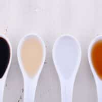 Four types of vinegar in spoons (sherry vinegar, red wine vinegar, white wine vinegar and apple cider vinegar).