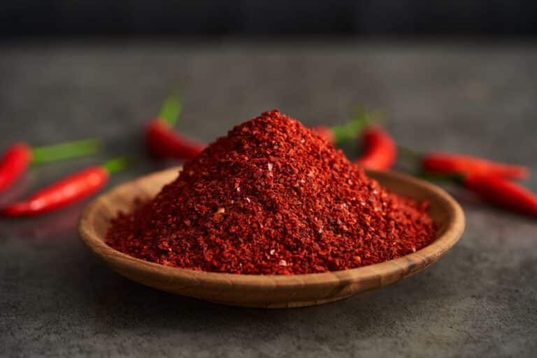 Cayenne peppers on a table and cayenne powder in a bowl.