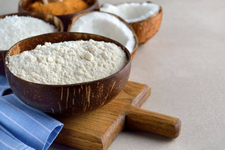 Coconut flour in a bowl next to coconuts.