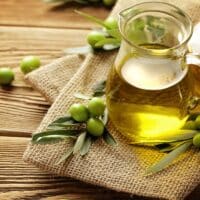 Olive oil in a glass jar next to olives.