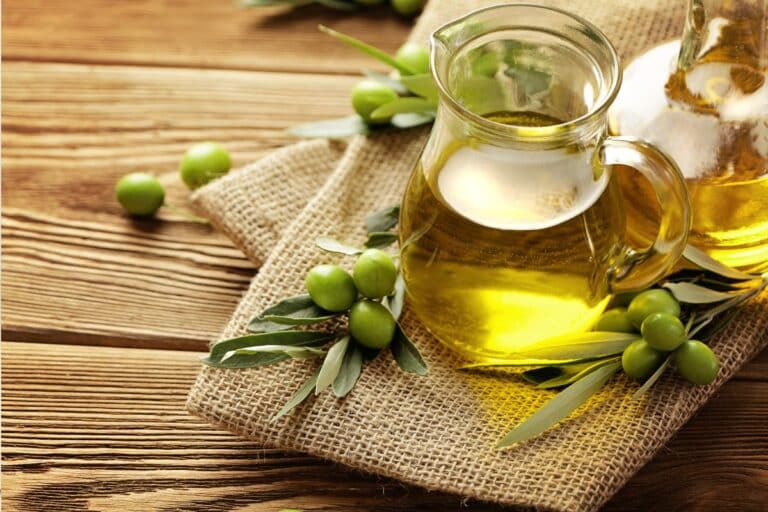 Olive oil in a glass jar next to olives.