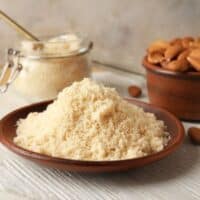 Almond flour in a bowl next to almonds.