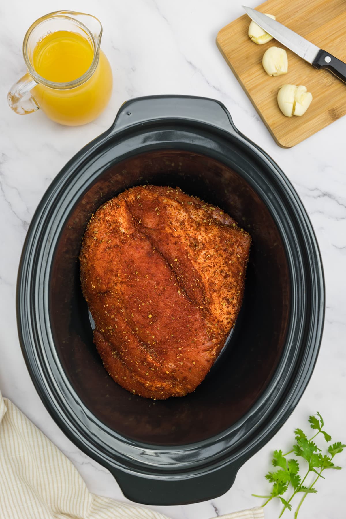 Pork shoulder covered with a spice rub in the slow cooker.