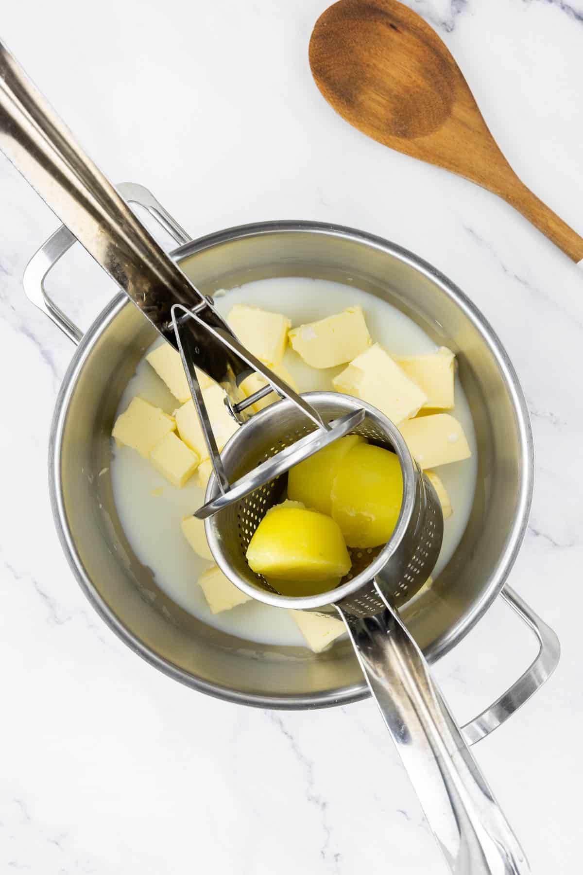 Using a potato ricer over a warm pot of butter and milk.