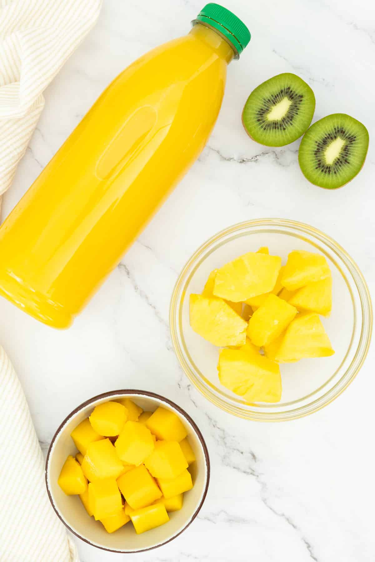 Mango, pineapple, kiwi and orange juice on a kitchen countertop.