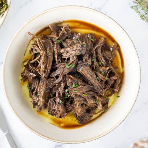 Slow cooker shredded beef in a bowl with mashed potato.